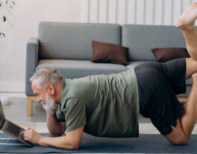Mature man doing yoga while looking at laptop for health and wellness tips article www.thetonic.co.uk