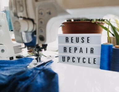 Reuse, repair, upcycle text on light board on sewing machines background. Stack of old jeans, Denim clothes, scissors, thread and sewing tools in sewing studio. Denim Upcycling Ideas, Using Old Jeans.